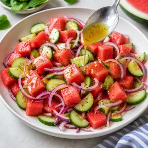 Dressing drizzled over watermelon, cucumber, and red onion