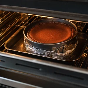 Baked chocolate cheesecake resting in a water bath inside the oven