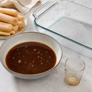 Coffee and coffee liqueur combined in a shallow bowl with a glass baking dish ready