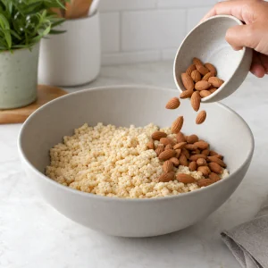 Roasted almonds being added to crisp rice cereal in a mixing bowl