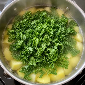 Kale picado repartido sobre trozos de papa hirviendo suavemente en una olla