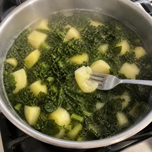 Kale y papas tiernos hirviendo suavemente mientras un tenedor prueba un trozo de papa