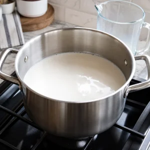 Whole milk poured into a large heavy bottomed pot on the stove