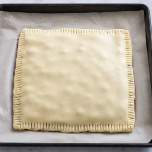 Top puff pastry sheet sealed over cherry filling with crimped edges