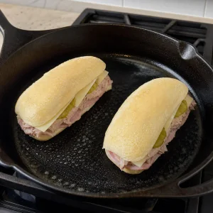 Dos sándwiches cubanos montados comenzando a cocinarse en una sartén de hierro