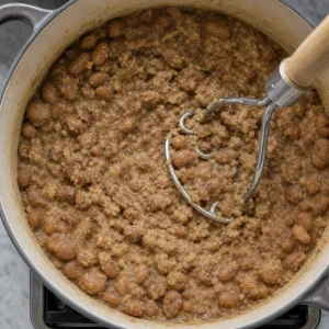 Cooked fava beans being partly mashed in the pot