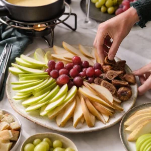 Sliced apples, pears, grapes, and dried figs arranged on a fondue platter