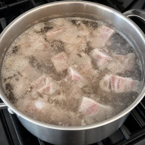 Schweinerippchen kochen in Wasser, während Schaum im Topf aufsteigt