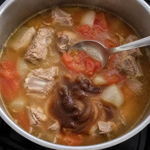 Tamarindenpaste löst sich in Schweinebrühe mit weichen Tomaten