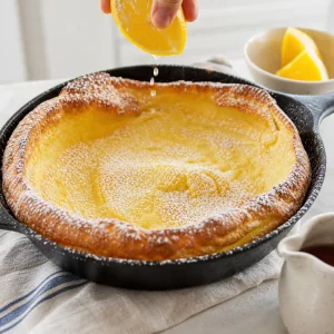 Finished German pancake dusted with powdered sugar and served with fresh lemon.
