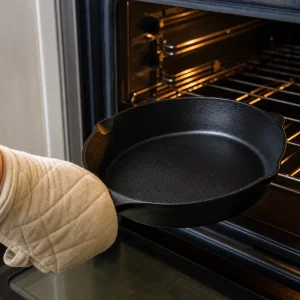 Hot empty cast-iron skillet being removed from the oven with a thick oven mitt.