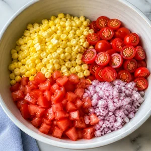 Corn, tomatoes, and chopped shallot arranged in a mixing bowl