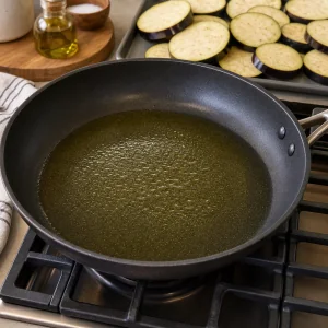 Olio d’oliva che si scalda in padella con fette di melanzana accanto