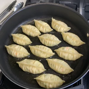 Raw pleated vegetable dumplings arranged in a single layer in an oiled skillet