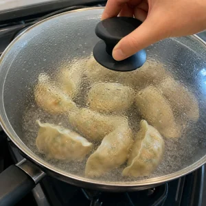 Vegetable dumplings steaming in a covered skillet with water bubbling around them