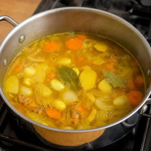 Golden ginger turmeric broth gently simmering with roots, carrots, onion, and bay leaves