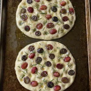 Unbaked focaccia topped with grapes, rosemary, sugar, and salt