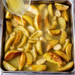 Lemon broth being poured over hot roasted potato wedges
