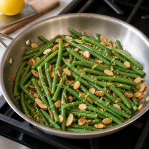 Judías verdes salteadas con almendras tostadas y ralladura de limón en una sartén.
