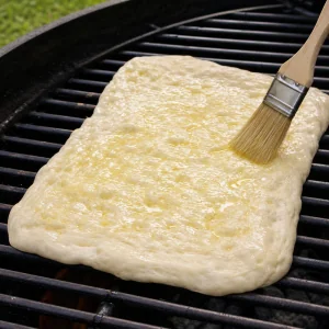 Impasto per pizza sulla griglia spennellato con olio all'aglio