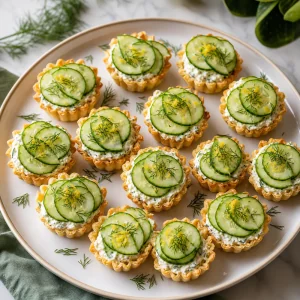 Tortinhas prontas de pepino com cream cheese de ervas arrumadas em uma travessa.