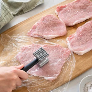 Filetes de cerdo sazonados y aplastados finos entre film plastico.