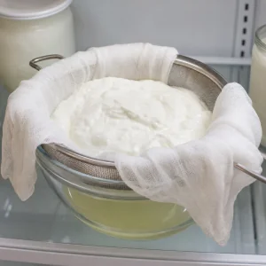Yogurt straining through cheesecloth in a sieve to become Greek style