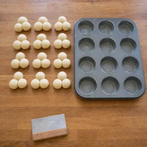 Thirty-six shaped dough balls beside a muffin pan