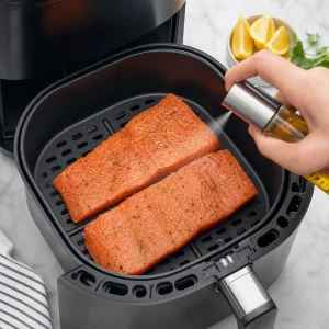 Salmone condito sistemato con la pelle verso il basso nel cestello della friggitrice ad aria e spruzzato con olio
