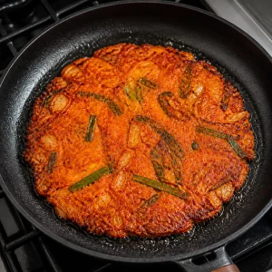 Kimchi pancake browning in a skillet with crisp edges