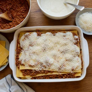 Lasagne wird mit Bolognese, Béchamel und Parmesan geschichtet