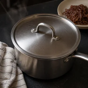 Covered saucepan resting off the heat with caramelized onions nearby