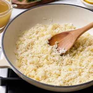 Отцеженный рис обжаривают с луком и чесноком до блеска перед тушением