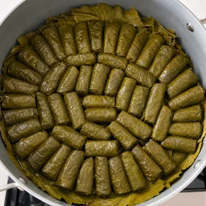 Фаршированные виноградные листья уложены швом вниз плотными концентрическими слоями в кастрюле