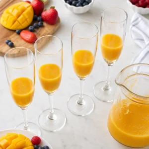 Vier Champagnerflöten zu einem Drittel mit goldenem Mangopüree gefüllt