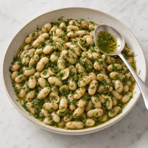 Marinated white beans in a shallow serving bowl with herb oil spooned over