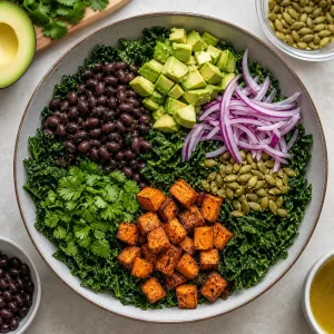 Couve kale com feijão preto, abacate, cebola roxa, sementes de abóbora, coentro e batata-doce assada.