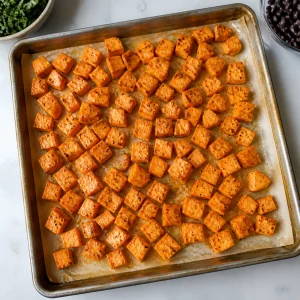 Cubos de batata-doce temperados espalhados em uma assadeira forrada.