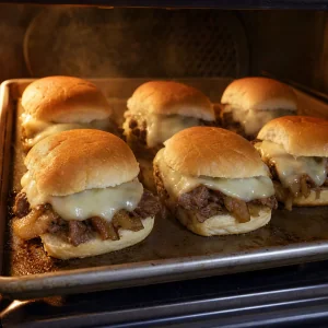 Mini cheesesteak sliders baking until the provolone melts