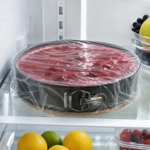 Cheesecake senza cottura coperta che si raffredda in frigorifero con copertura rossa visibile
