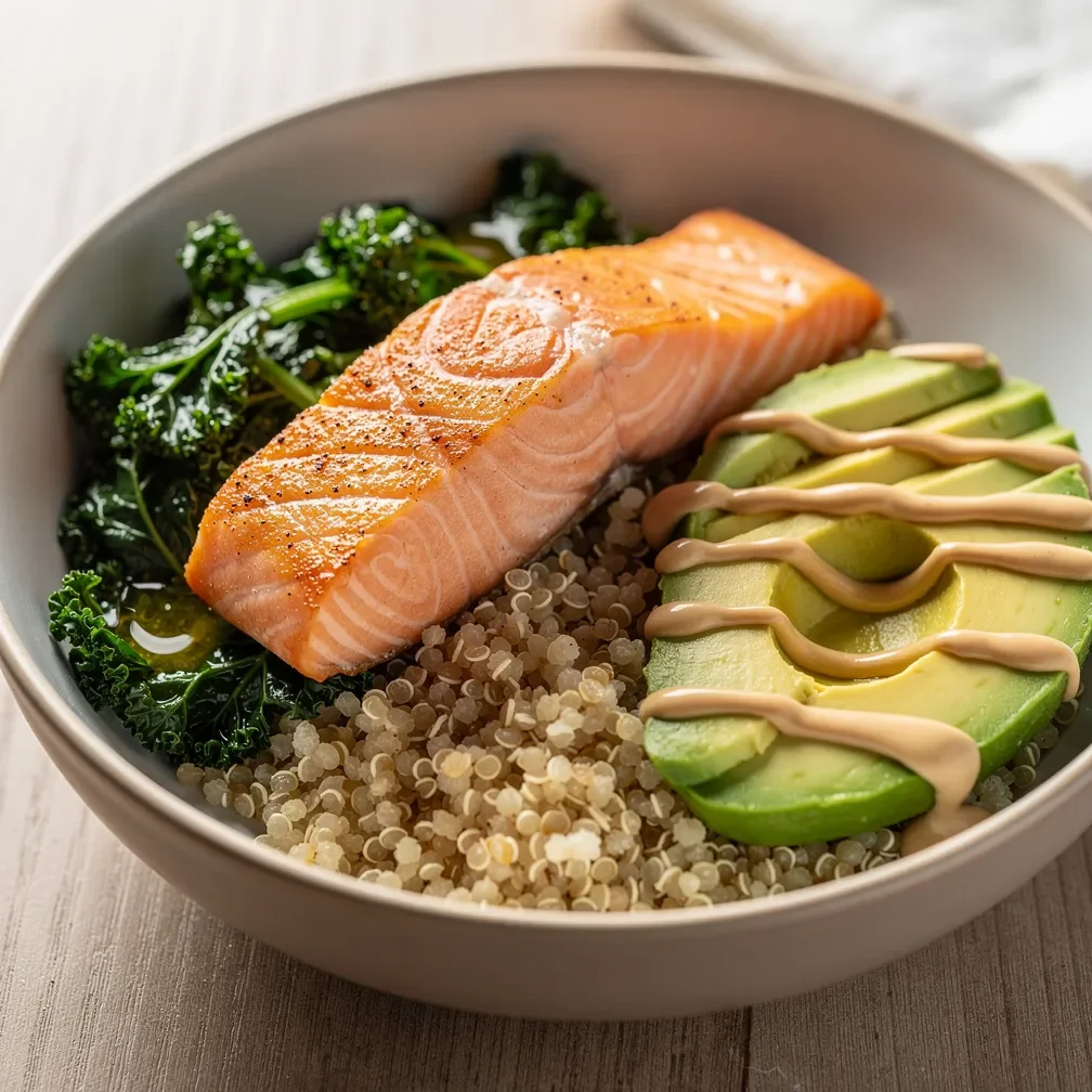 A nourishing bowl with pan-seared salmon, quinoa, sautéed kale, and sliced avocado