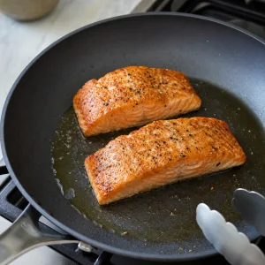 Seasoned salmon fillets searing in olive oil until golden