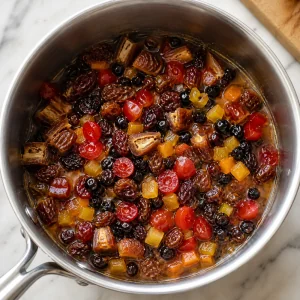 Dried fruit and candied cherries soaking in a saucepan