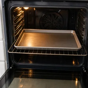 A rimmed baking sheet warming on the middle rack inside an oven.