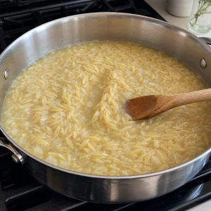 Orzo simmering uncovered in glossy broth