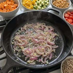 무쇠 팬에서 적양파와 마늘이 올리브유에 볶아지고 있습니다.