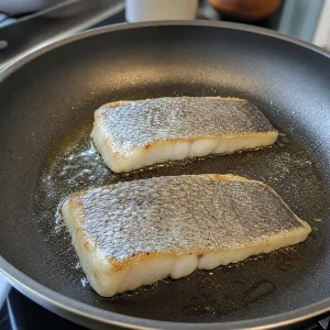 Barramundi fillets searing skin-side down in olive oil