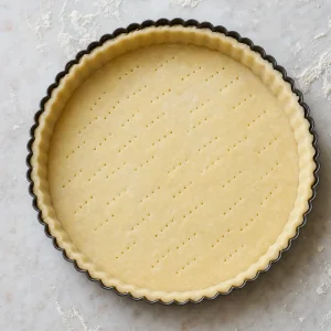 Raw tart shell pricked with fork holes in a fluted pan