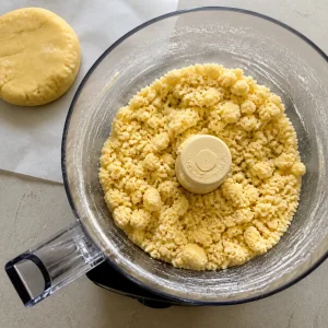 Tart dough clumps in a food processor with a dough disk nearby