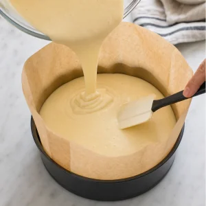 Smooth cheesecake batter poured into the tall parchment-lined pan